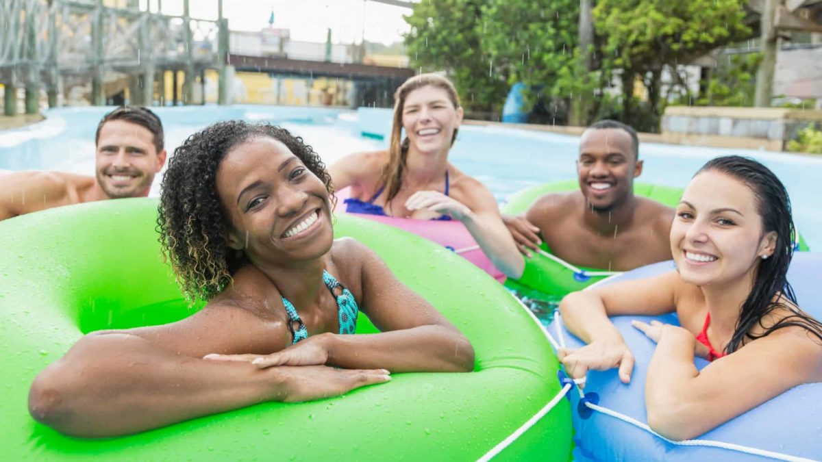 five people in colourful blow up tubes in a resort style pool gather and smile in a relaxed holiday picture.