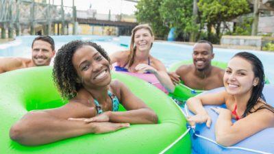 five people in colourful blow up tubes in a resort style pool gather and smile in a relaxed holiday picture.