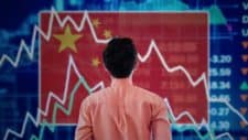 a man looks at a stock exchange graph board backgrounded by a Chinese flag