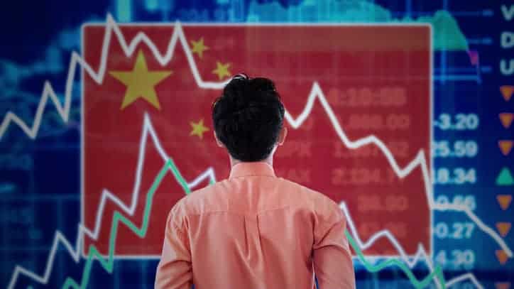 a man looks at a stock exchange graph board backgrounded by a Chinese flag