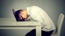 a man sitting at a desk slumps forward to put his head on his laptop computer in a gesture of failure, devastation or hopelessness.