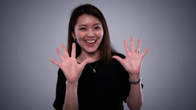 A woman with a broad smile on her face holds up ten fingers.