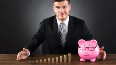 Young male investor with a pink piggy bank and pile of gold coins