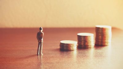 miniature figure of man standing in front of piles of coins