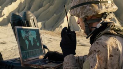 soldier talking into wireless radio whilst working on laptop computer