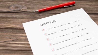 Checklist page on wooden table with red pen