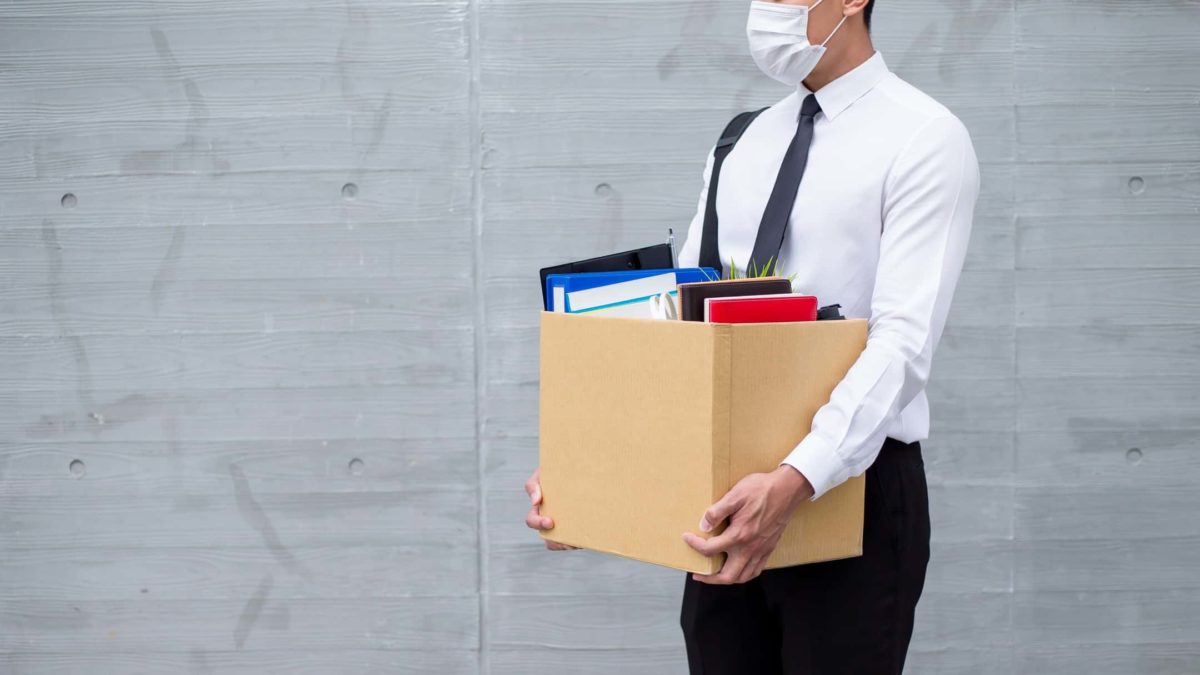 Recently unemployed man in white business shirt wearing face mask carrying box of belongings
