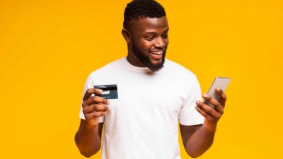 Man in white t-shirt holding Visa card and mobile in front of yellow background