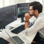 Worried young male investor watches financial charts on computer screen