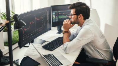 Worried young male investor watches financial charts on computer screen