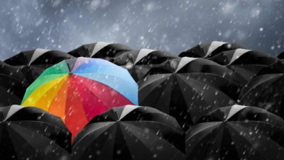 colourful striped umbrella amidst all black umbrellas