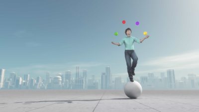 man standing on concrete ball juggling small coloured balls