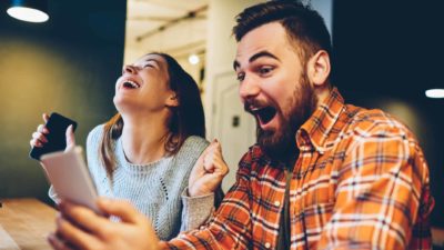 man and woman looking at mobile phones in a celebratory manner