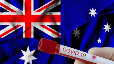 gloved hand holding covid-19 vaccine against backdrop of australian flag