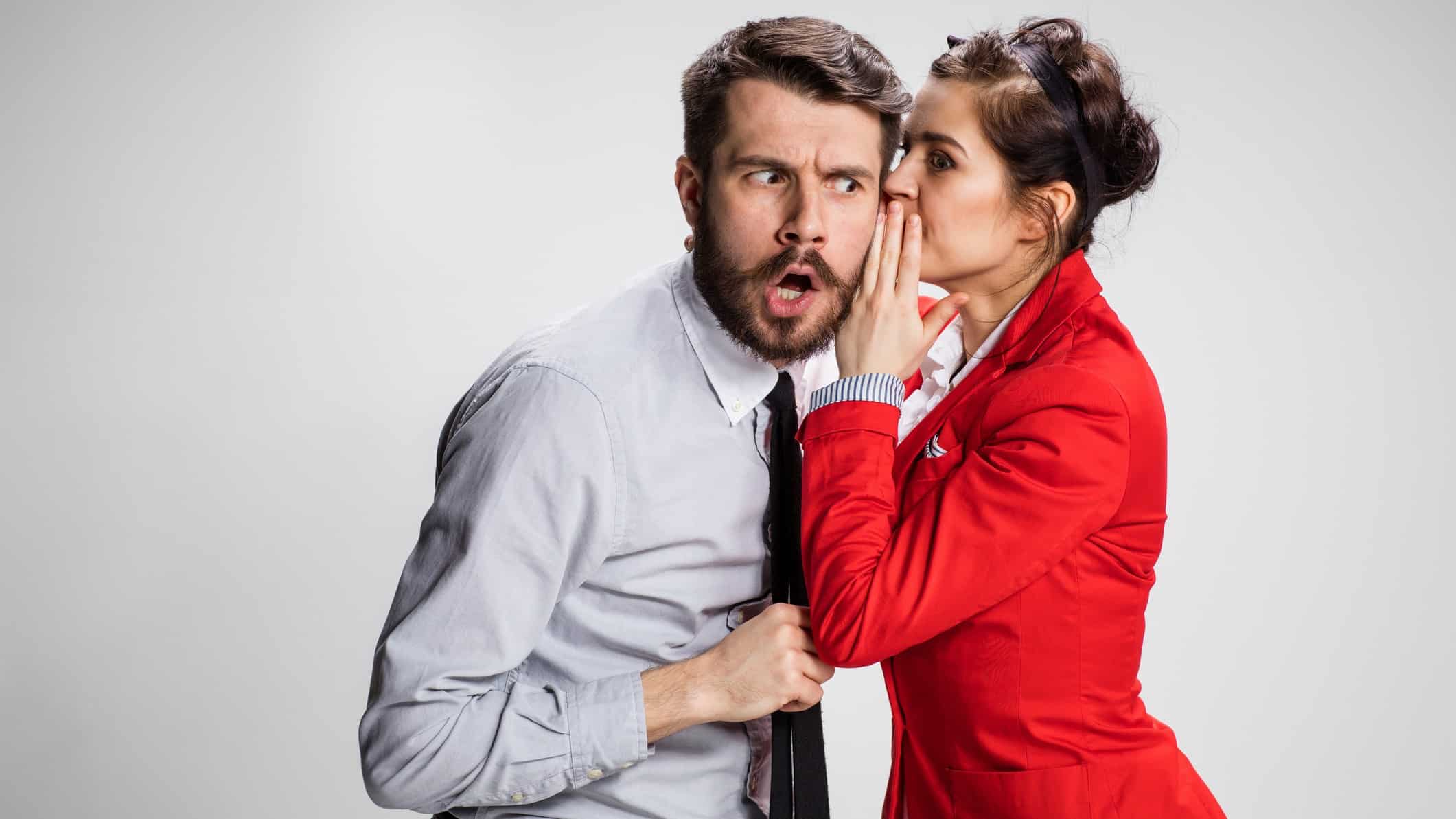 A female broker in a red jacket whispers in the ear of a man who has a surprised look on his face as she explains which two ASX 200 shares should do well in today's volatile climate