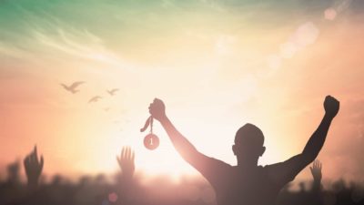 man holding 1st place medal against backdrop of sunset