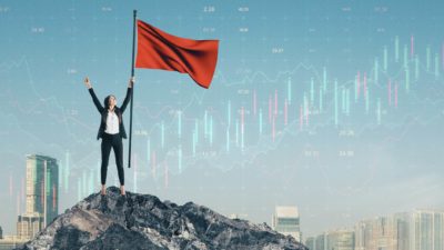 woman holding flagpole on top of peak against backdrop of city and stock chart, representing a share price high
