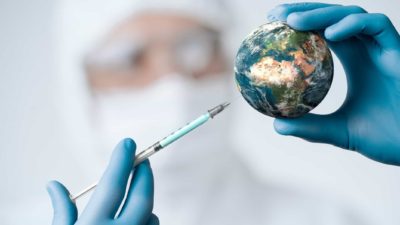 Doctor holding small world globe in one hand and a Covid vaccine needle in the other