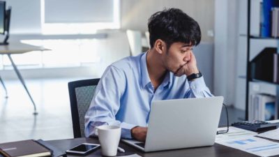 Falling ASX share price represented by young male investor sitting sadly in front of a laptop.