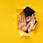 asx share price secret represented by woman holing hands up to ear through hole in wall