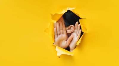 asx share price secret represented by woman holing hands up to ear through hole in wall