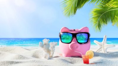 Piggy bank on tropical island with sunglasses on, sipping a fruity cocktail