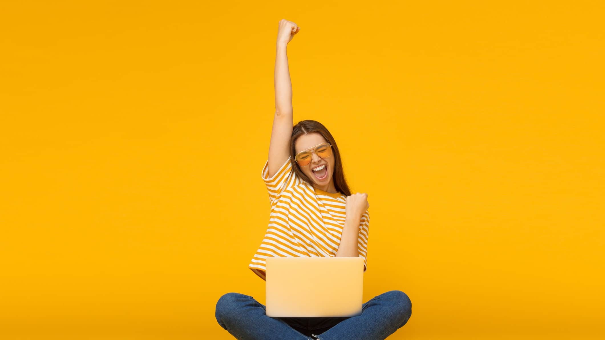 Young woman in yellow striped top with laptop raises arm in victory
