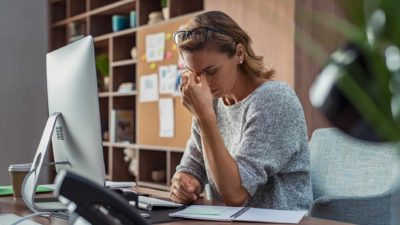 Female investor in front of computer with hands at forehead.