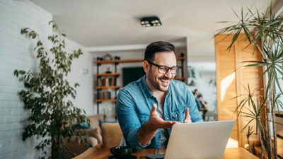 A man sits at his dining table looking at his laptop with a surprised look on his face