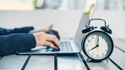 Alarm clock sitting on table next to man typing on laptop