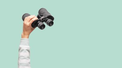 Woman with binoculars on green background, looking through binoculars, journey, find and search concept.