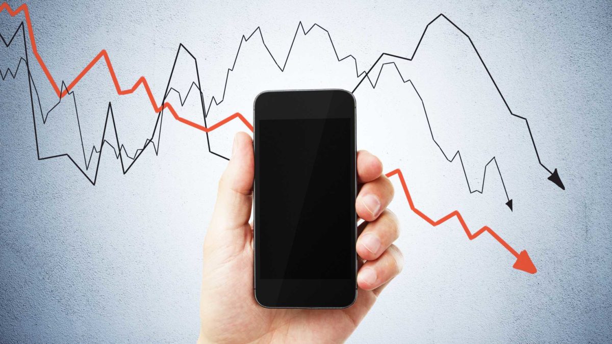 hand holding mobile phone against back drop of line chart representing Telstra share price split restructure