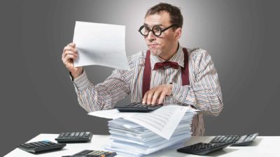 A man wearing thick rimmed black glasses and a business shirt with red suspenders sits at his desk sorting through the earnings report of Nickel Mines