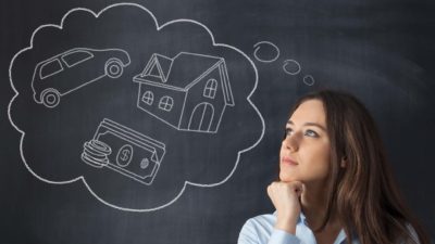 woman standing in front of blackboard with thought bubble containing car, house and money