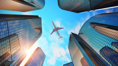 view from below of jet plane flying above city buildings representing corporate travel share price