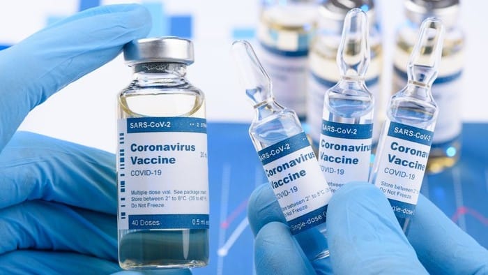 Blue gloved hands holding up vials with covid vaccine labels