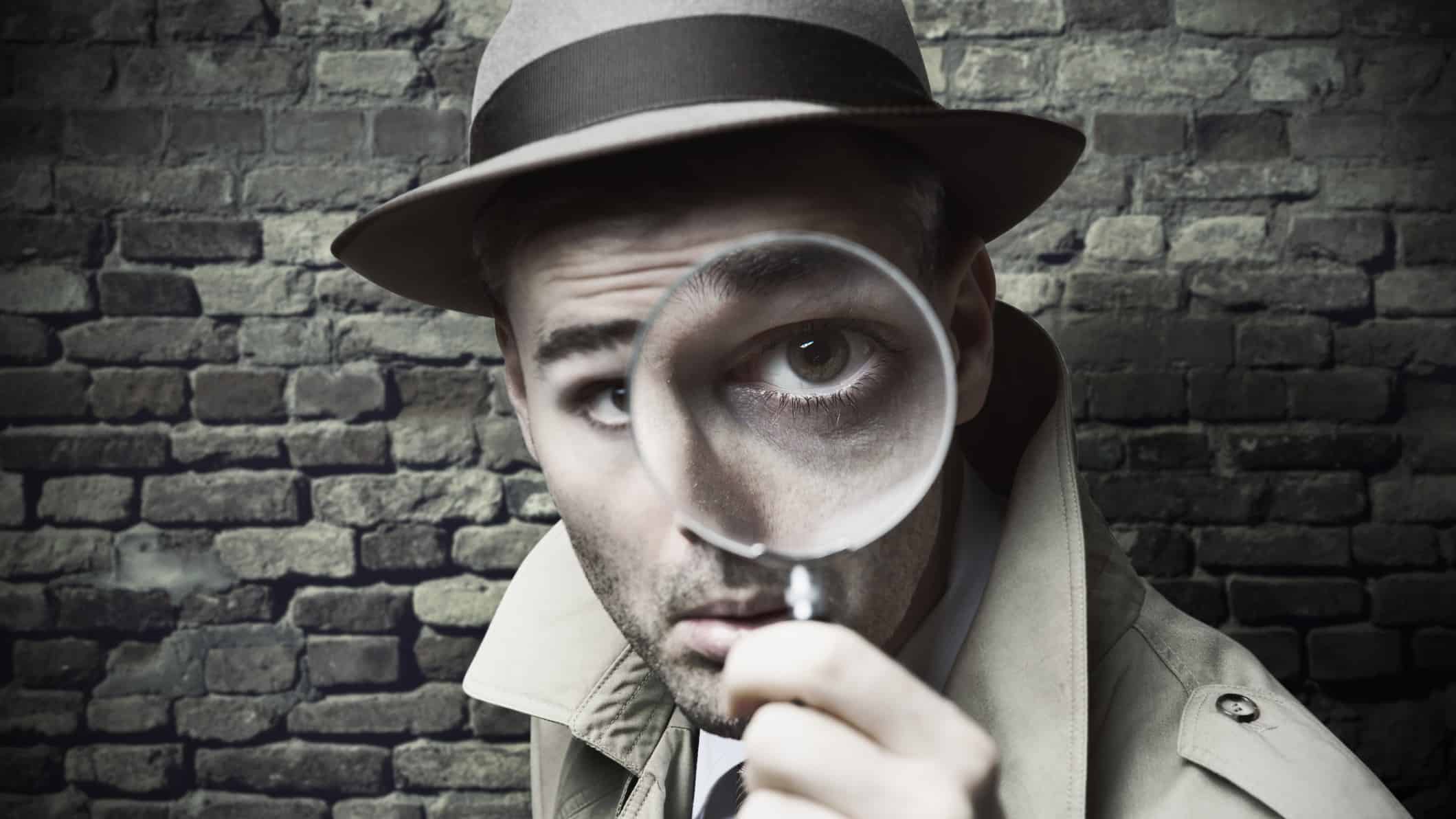 man in old fashioned suit and hat looking through magnifying glass
