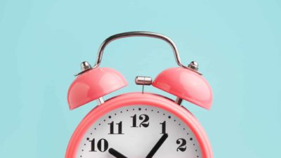 close up of pink alarm clock against blue background