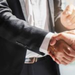 2 businessmen shaking hands, indicating a partnership deal and share price lift