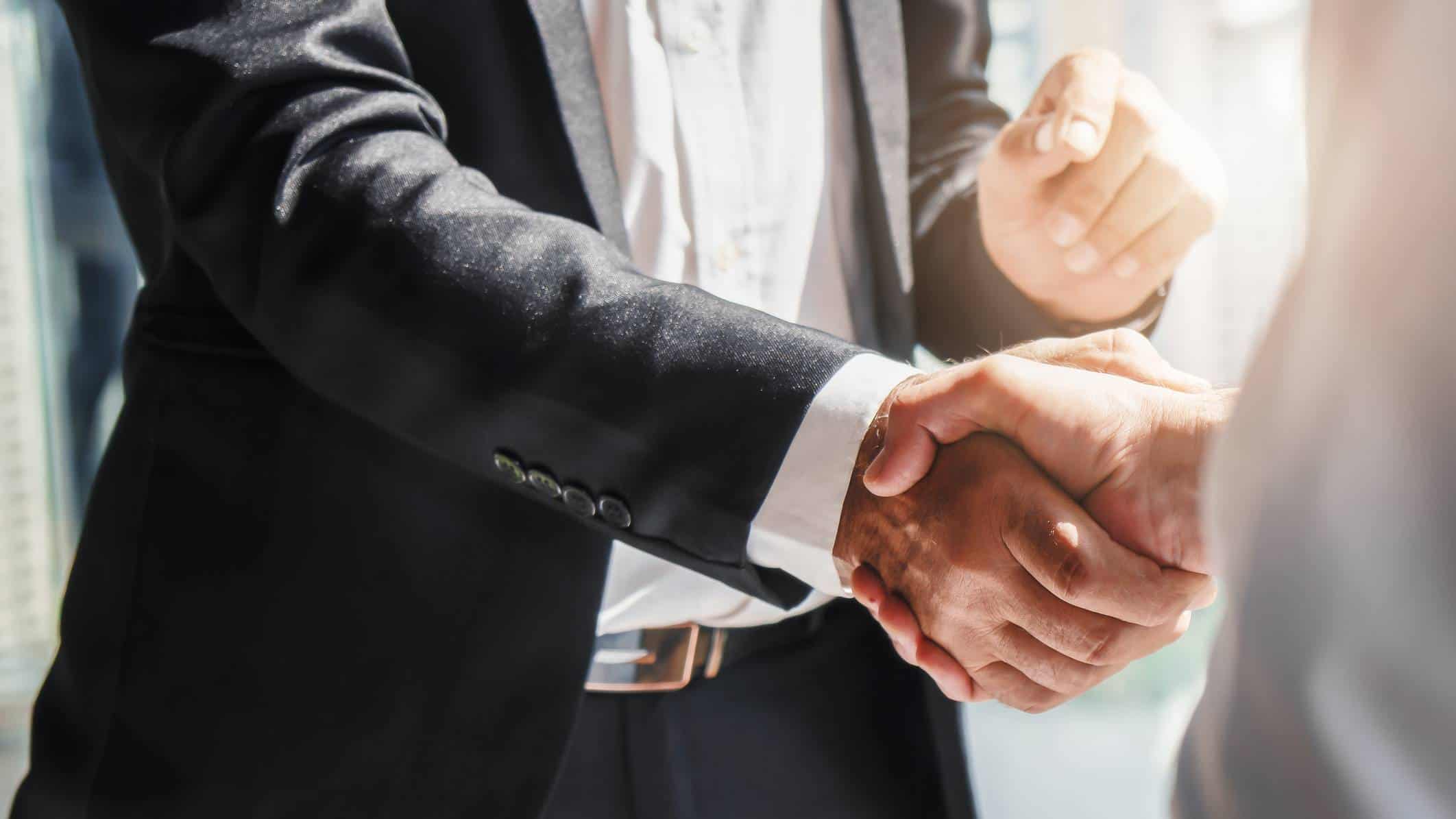 2 businessmen shaking hands, indicating a partnership deal and share price lift