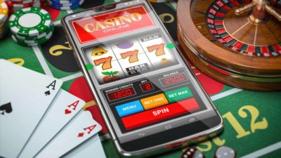 mobile phone depicting online casino next to cards, casino chips and roulette wheel