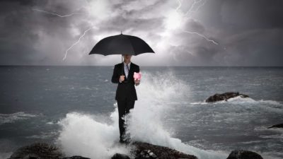man holding piggy bank under umbrella during a storm