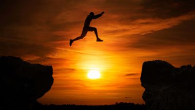 man leaping from one cliff to another against sunset backdrop