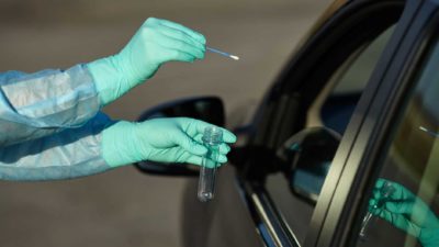 pair of gloved hands holding cotton swab and test tube towards car window representing Anteotech share price