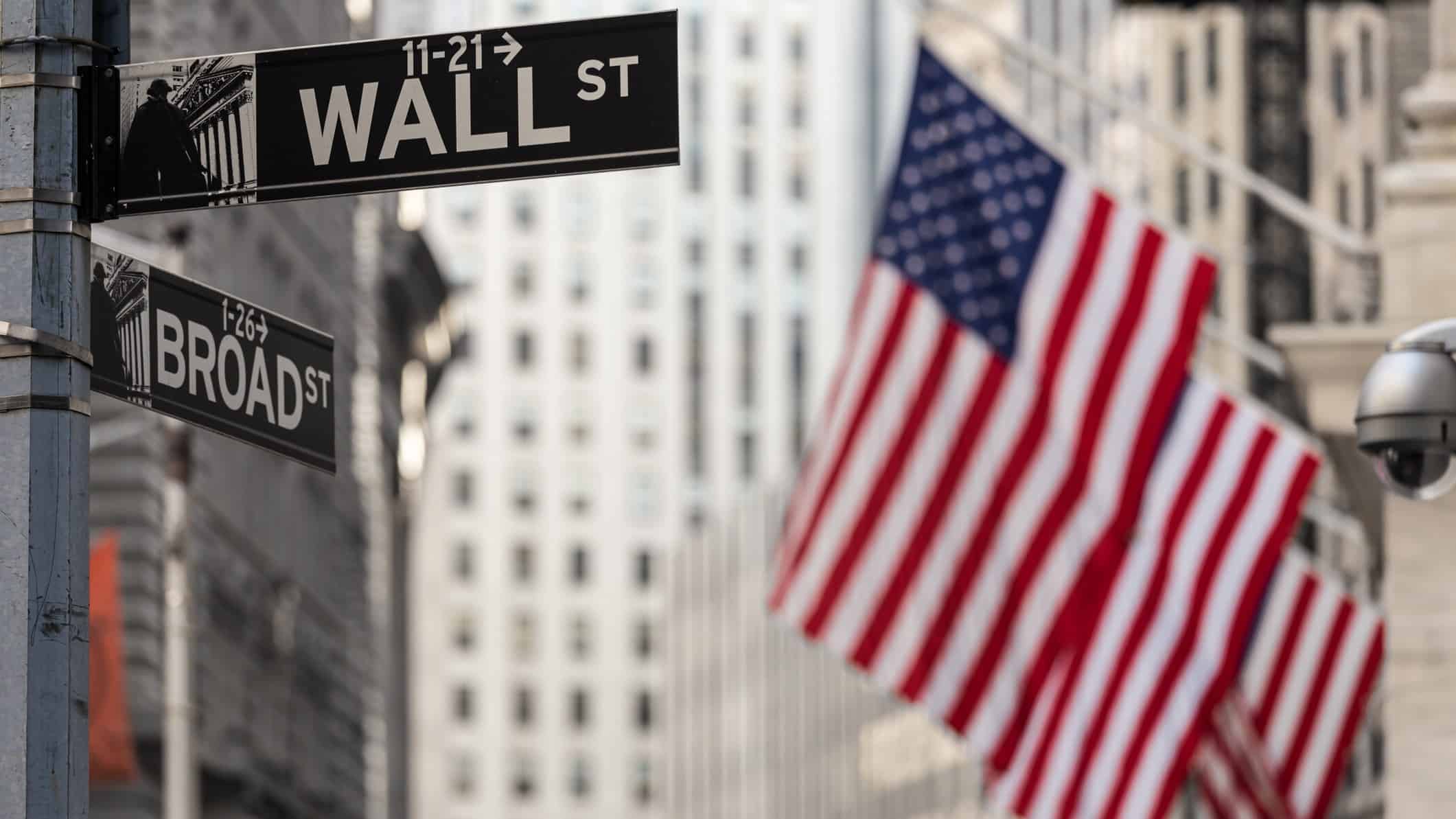 Road sign for 'Wall St' with US flags in background