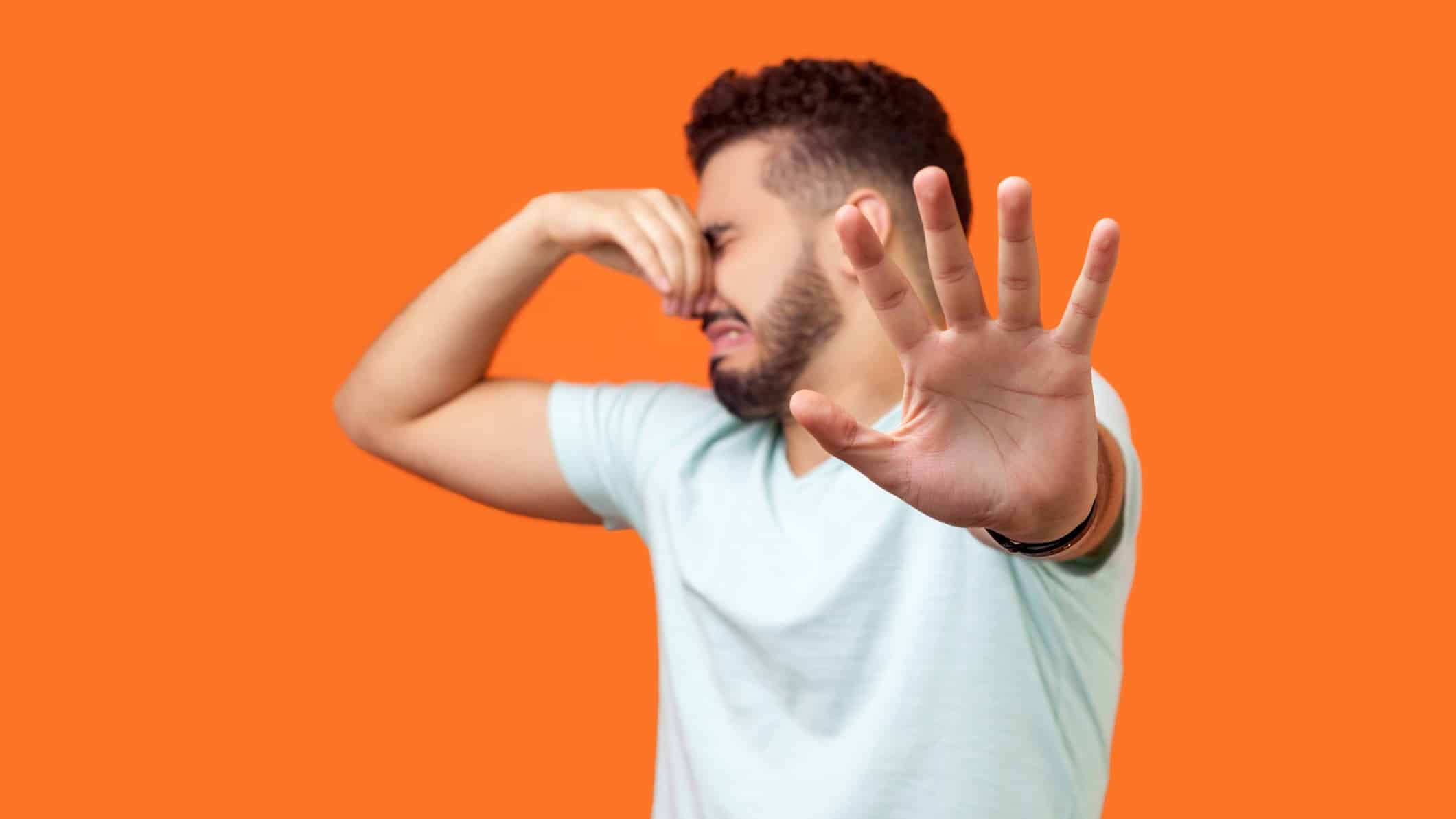 Man pinching nose and holding other hand up in a 'stop' gesture turning away in front of an orange background