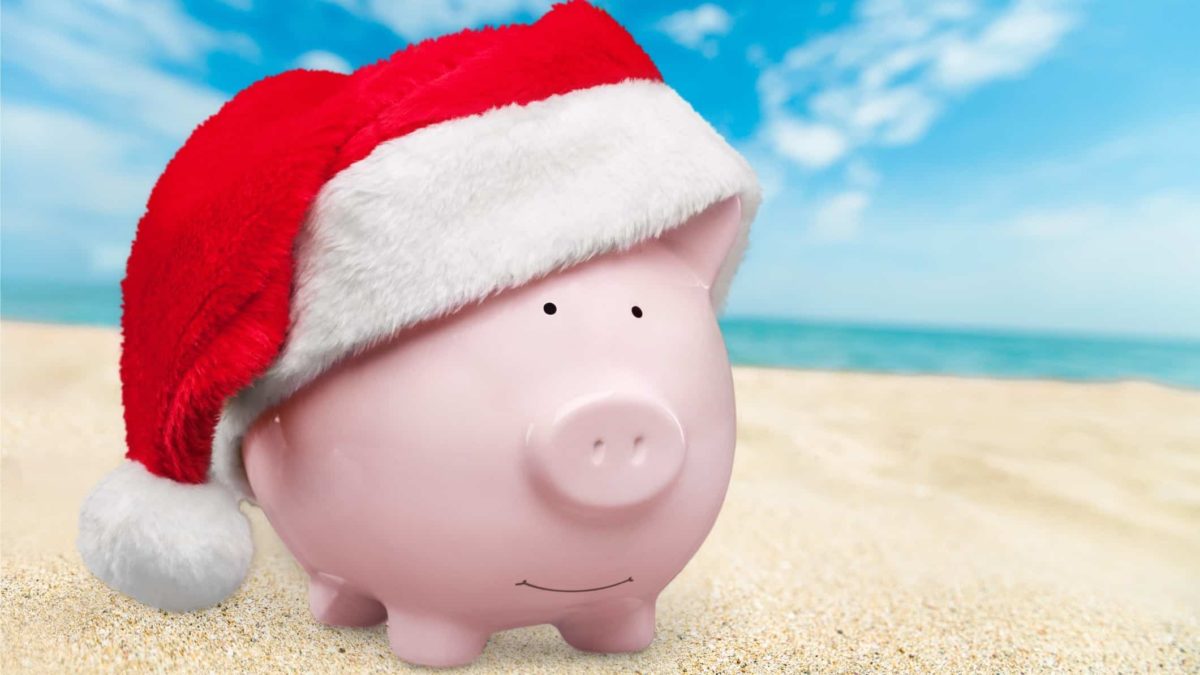 piggy bank sitting on beach wearing christmas hat and representing asx share