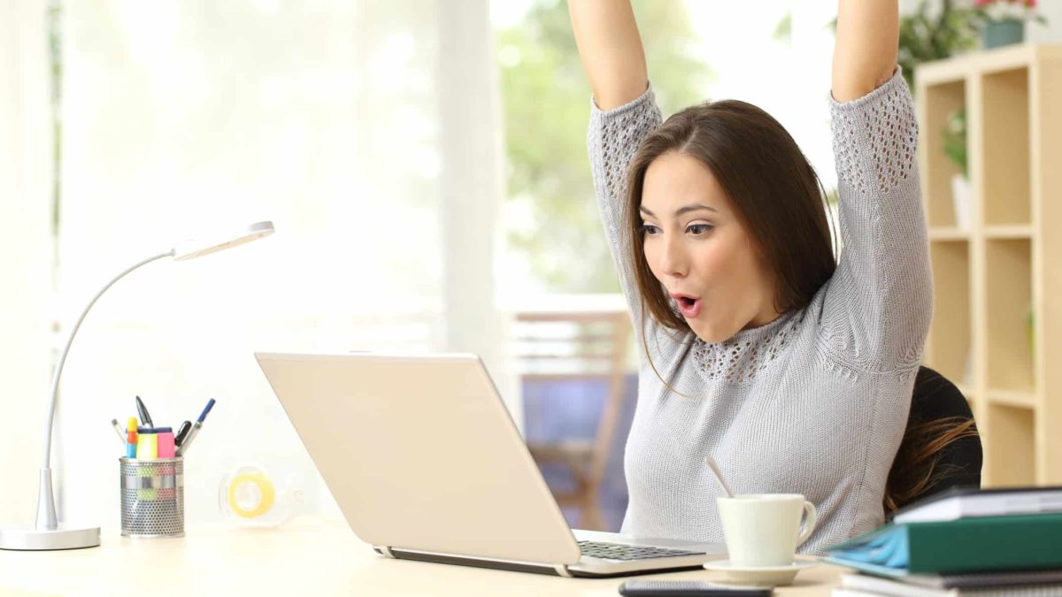 An investor sits at her desk and stretches her arms above her head in delight.