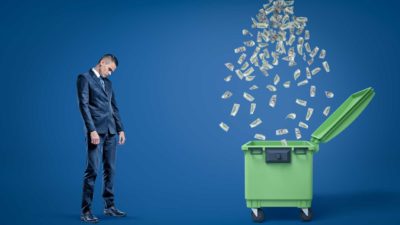 man standing next to garbage bin with money falling into it representing falling cleanaway share price