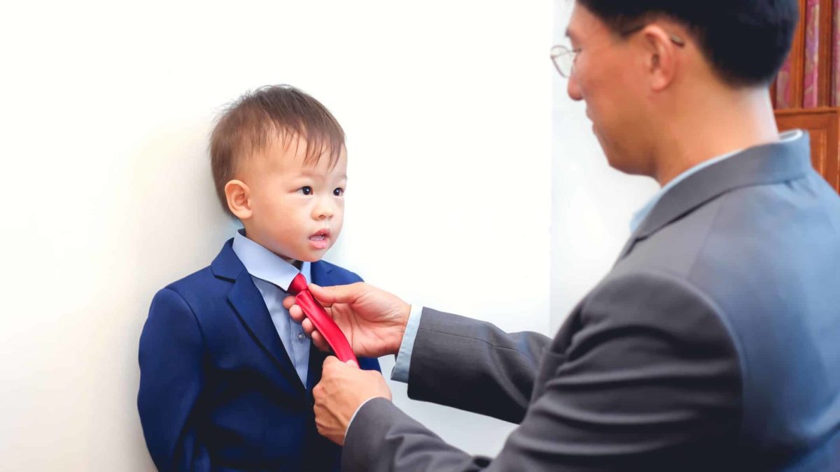 business man adjusting suit and tie on his young son representing a family business